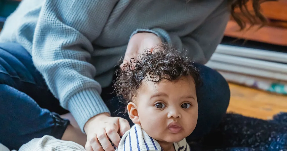 An adult supervising an awake baby lying on their tummy on the floor