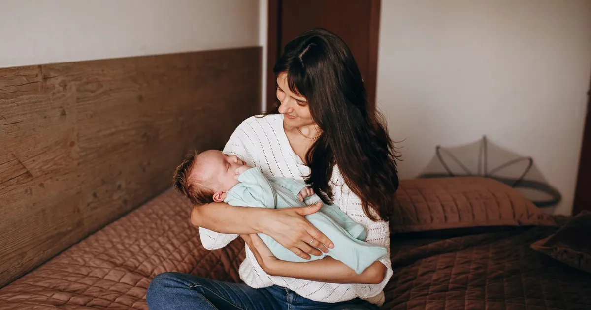 An adult sitting on a bed holding a newborn