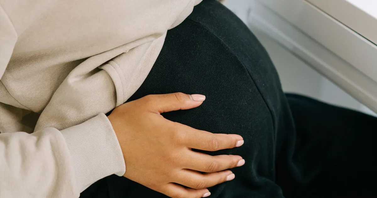 A pregnant person resting their hands on their belly while seated