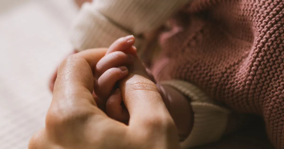 An adult gently holding a newborn’s hand
