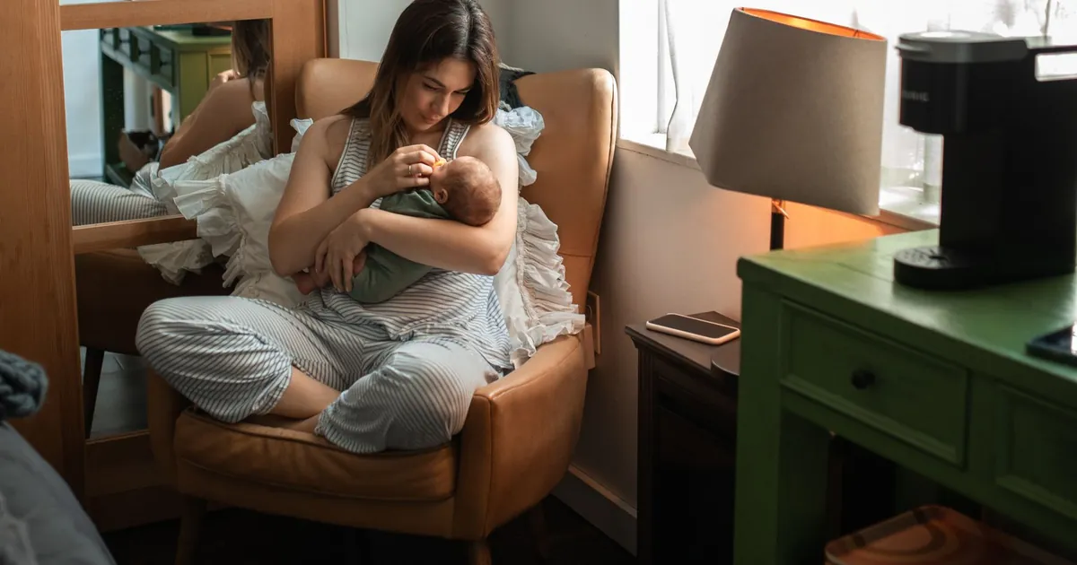 An adult sitting by a window holding a baby